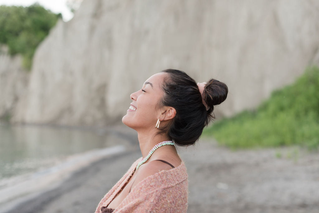 woman happy at beach wearing gold hoop earrings and gemstone necklaces