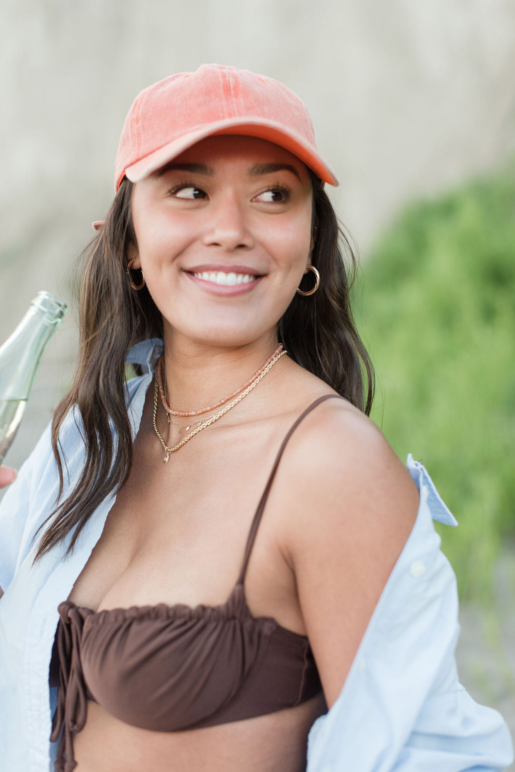 Woman with baseball cap and water bottle at the beach in gold jewelry